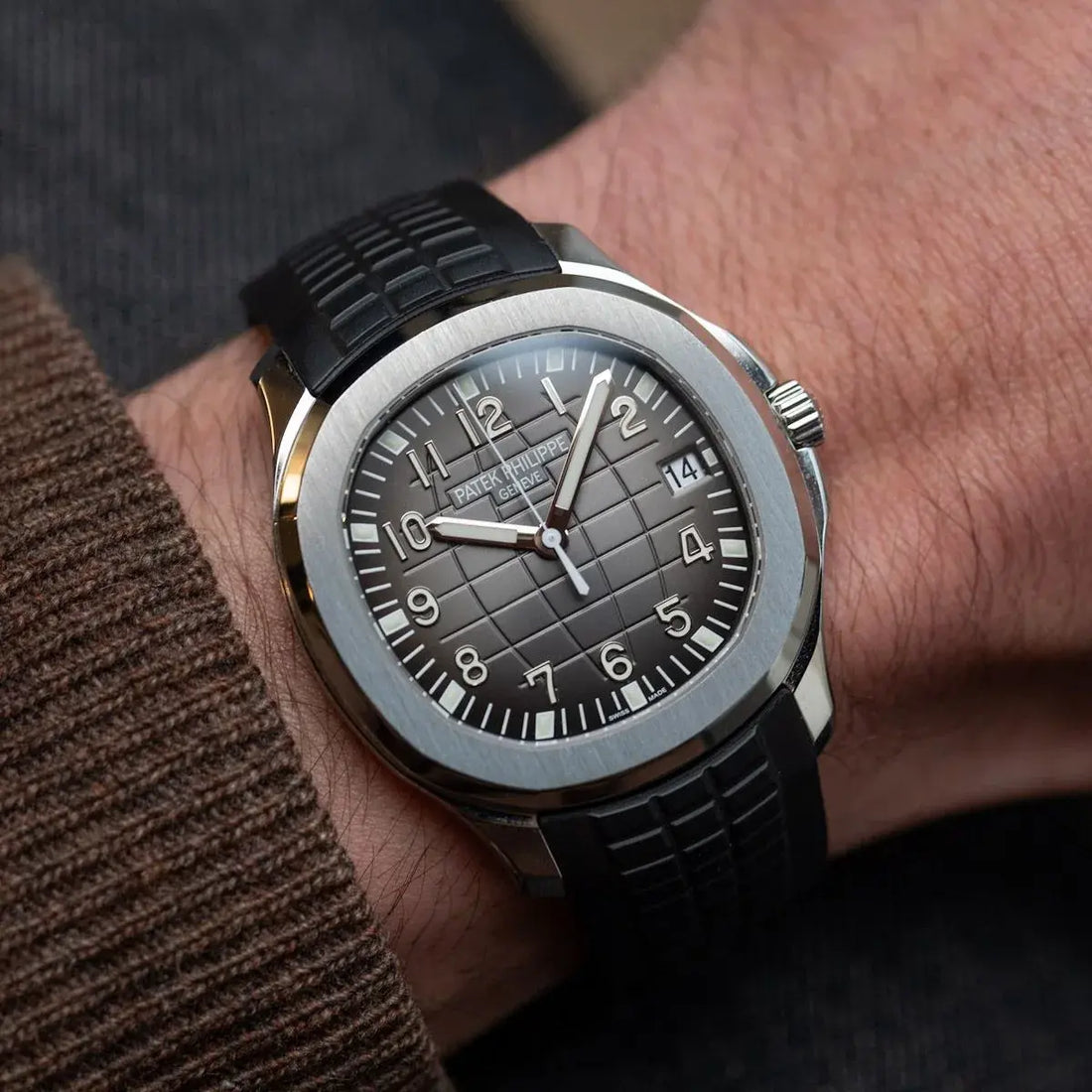 Gros plan sur une montre de luxe Patek Philippe Aquanaut portée au poignet, cadran gris texturé et bracelet en caoutchouc noir, haute résolution.