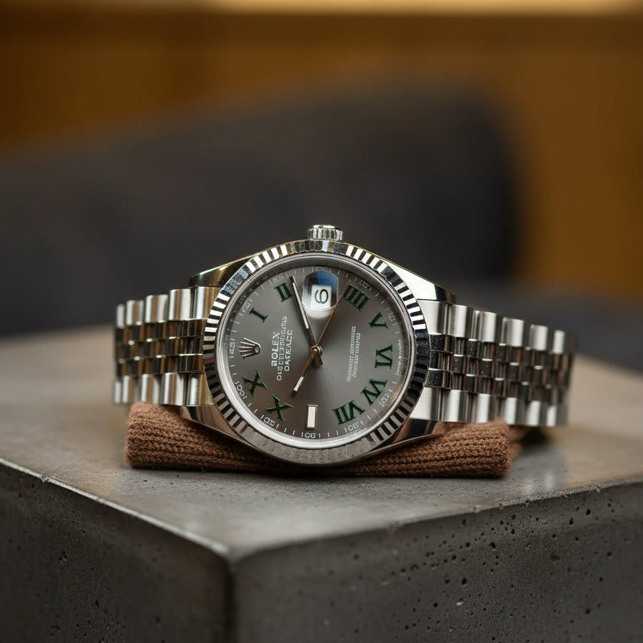Montre de luxe Rolex Datejust avec cadran Wimbledon gris et chiffres romains verts, lunette cannelée en acier sur un socle en béton, photographie haute résolution pour blog horloger.